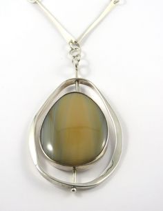 This is a modern designed sterling silver bezel set swivel Agate pendant with a 24 inch chain. The large tear shaped cabochon cut agate has various hues of light brown and gray colors in it and is bezel set. The outer egg shaped silver border is attached to the center with a silver bar that  allows the pendant to swivel. The back of the pendant is closed and is signed " rme sterling 1975". The 24 inch chain is made up of long twisted silver bars and each link is connected by  large round jump ri Modern Jewelry With Polished Teardrop Finish, Modern Teardrop Jewelry With Polished Finish, Unique Drop Jewelry With Polished Finish, Modern Sterling Silver Jewelry With Large Stone, Unique Oval Necklace With Polished Finish, Contemporary Teardrop Jewelry For Gift, Modern Teardrop Necklace With Polished Finish, Modern Oval Necklace With Polished Finish, Modern Jewelry With Large Oval Stone