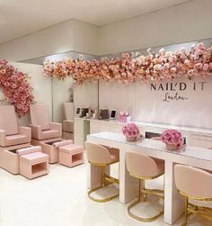 the interior of a nail salon with pink chairs and flowers hanging from the wall above it