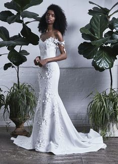 a woman in a white wedding dress standing next to some potted plants and greenery