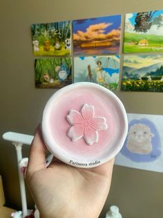 a person holding up a small pink candle with a flower on it in front of some pictures