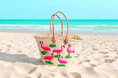 a pink flamingo purse sitting on top of a sandy beach next to the ocean