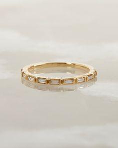 a yellow gold band with baguets on the side, sitting on a white surface