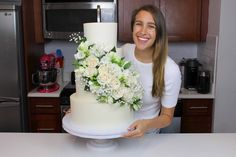 a woman standing next to a cake with flowers on it