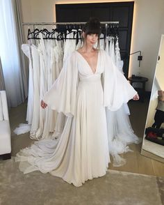 a woman standing in front of a mirror wearing a white dress and cape over her shoulders