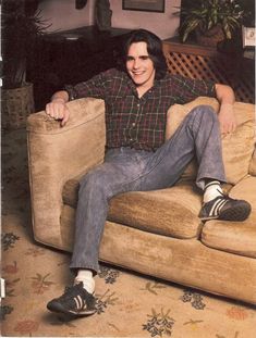 a man sitting on top of a couch in a living room next to a plant