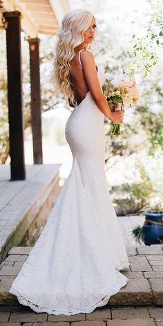 a beautiful blonde woman in a white wedding dress standing on the steps with her back to the camera