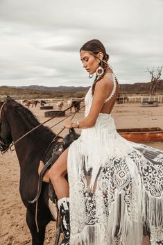 a woman sitting on top of a black horse in the desert with other animals behind her