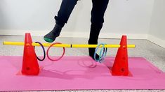 a person standing on top of a pink mat next to red cones and orange poles