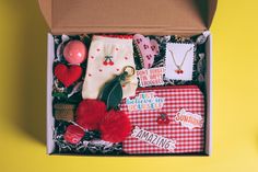 an open box filled with assorted items on top of a yellow table next to a red and white checkered cloth