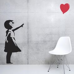 a white chair sitting in front of a wall with a red heart painted on it