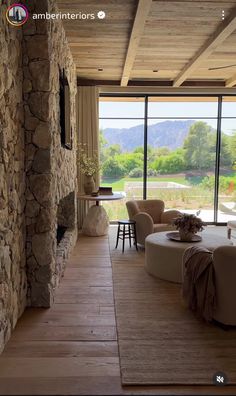 a living room with stone walls and flooring next to a large window overlooking the mountains