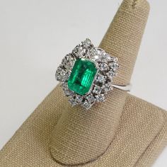 This Platinum Vintage Ring has a stunning large emerald as its center piece. The emerald has strong intense green color and shimmers as you move the piece around! The emerald is set with prongs and on all sides surrounded with sparkly high quality eye clean diamonds in flower petal shapes. There are a total of 57 round brilliants for a total of 2 carats. The ring is a size 7.5. This ring is a great collector's piece with its sparkly flowery design and good quality large emerald! Ring Size: 7.5 T Platinum Baguette Cut Green Emerald Ring, Emerald Ring With Halo Setting In Platinum, Exquisite Green Emerald Ring With Halo Setting, Exquisite Green Emerald Platinum Ring, Green Emerald Platinum Ring With Halo Setting, Green Emerald Ring With Halo Setting In Platinum, Green Platinum Emerald Ring For May Birthstone, Exquisite Green Emerald Diamond Ring, Luxury Green Emerald Ring With Center Stone