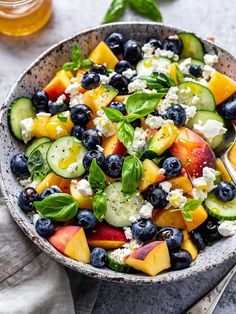 a bowl filled with blueberries, cucumber, peaches and other fruits