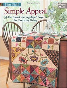 a table with a quilt on it next to a chair and vase filled with flowers