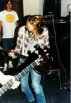 a young man is playing an electric guitar while another plays the bass in front of him