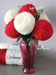 red and white crochet roses in a vase with yarn on the table next to it