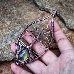 a hand holding a wire wrapped broochle on top of a stone wall next to a rock