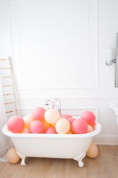 a bathtub filled with pink and white balloons on top of a hard wood floor