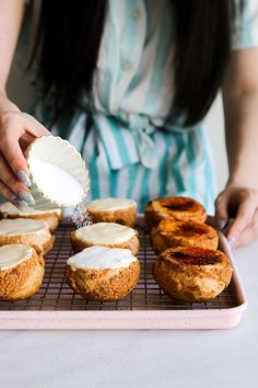 a woman is spreading icing on some baked goods