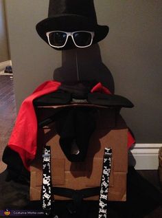 a cardboard box with a black hat and glasses on it, sitting in front of a wall