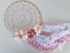 there is a white doily with pink flowers on it next to a piece of lace