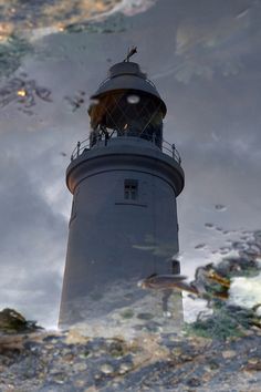 a reflection of a lighthouse in the water with rocks and grass on the ground behind it