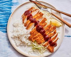 a white plate topped with rice and meat covered in ketchup next to a fork