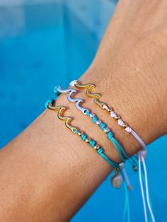 a woman's arm with three bracelets on it, next to a swimming pool