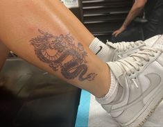 a person with a dragon tattoo on their leg sitting down and holding onto a shoe