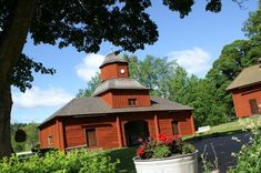 a red building with a clock tower on the top is surrounded by greenery and trees