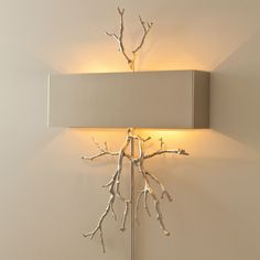 a white wall with two branches on it and a light fixture in the corner between them