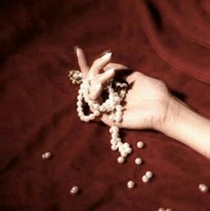 a woman's hand holding beads and making a peace sign with her fingers on a red cloth