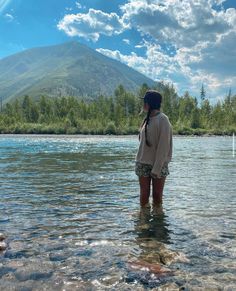 a woman standing in shallow water with mountains in the background