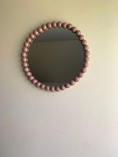 a round mirror mounted on the wall above a wooden bead necklace hanging from a hook