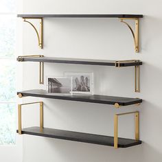 two black and gold shelves in a white room with a window behind them, one shelf has an empty photo on it