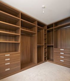 an empty walk - in closet with wooden shelves and drawers on the wall, carpeted floor