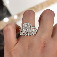 a woman's hand with a diamond ring on top of her wedding band and an engagement ring in the middle