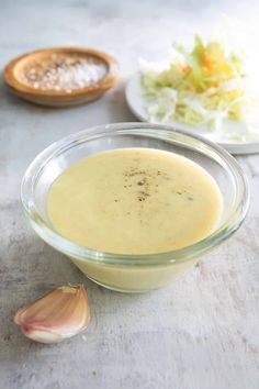 a glass bowl filled with soup next to an onion and lettuce salad on a table