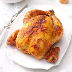 a chicken on a white plate next to a fork and knife