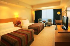 a hotel room with two beds, television and chair in front of a large window