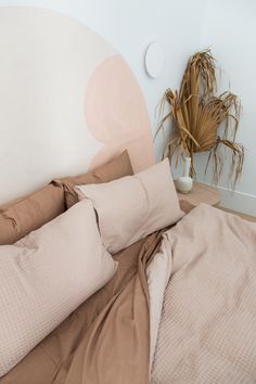 an unmade bed with two pillows and a plant in the corner