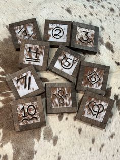 six wooden squares with numbers and symbols on them sitting on a cow hide area rug