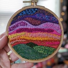 a person holding up a small embroidery hoop with mountains in the background and trees on it