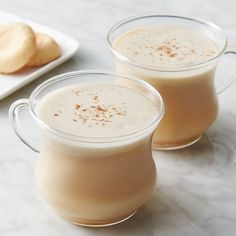 two glasses filled with liquid sitting on top of a table next to cookies and a plate