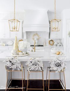 a white kitchen with gold accents and decorations on the countertop, along with four chairs