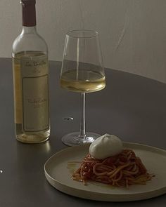 a plate with spaghetti and a bottle of wine sitting on a table next to it