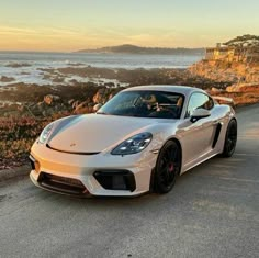 a white sports car is parked on the side of the road near the water and rocks