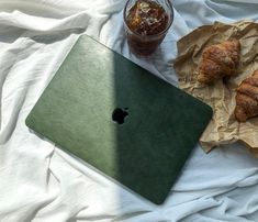 an apple laptop and some croissants on a white sheet next to a drink