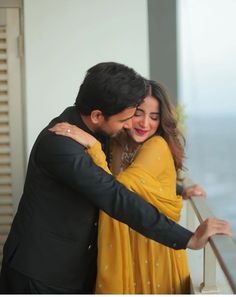 a man and woman hugging each other in front of a window with the ocean behind them