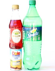 two bottles of soda sit next to each other on a white surface, one is green and the other is red